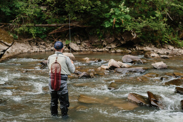 Fisherman catching trout in river, fly fishing in mountain stream
