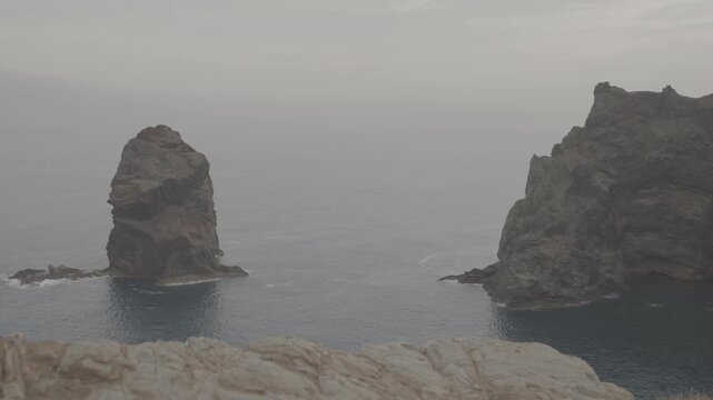 Wide shot of tall sea stacks and volcanic cliff in Madeira Portugal against calm ocean backdrop (SLOG3)