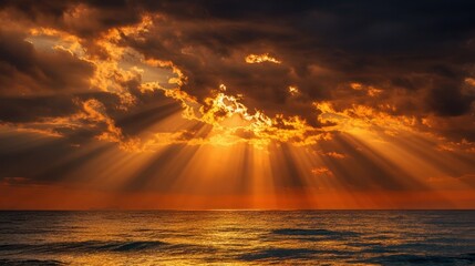 Bright orange and yellow hues fill the sky as the sun sets over the ocean. Clouds create a dramatic scene with rays of light illuminating the water creating a peaceful atmosphere at dusk.
