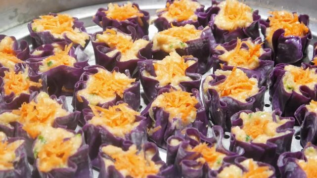 Homemade purple chicken dim sum with grated carrots on top arranged neatly on a stainless steel steamer