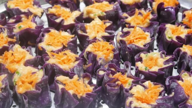 Homemade purple chicken dim sum with grated carrots on top arranged neatly on a stainless steel steamer