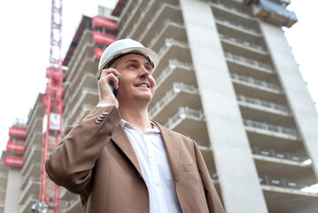 Fototapeta premium Smiling construction manager talking on phone at building site in city area.