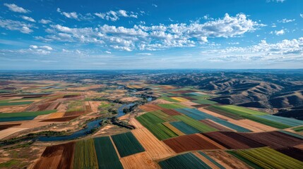 Aerial view of expansive colorful patchwork farmland with cultivated fields, vibrant crop patterns, distant rolling hills, blue sky with scattered clouds, scenic rural landscape