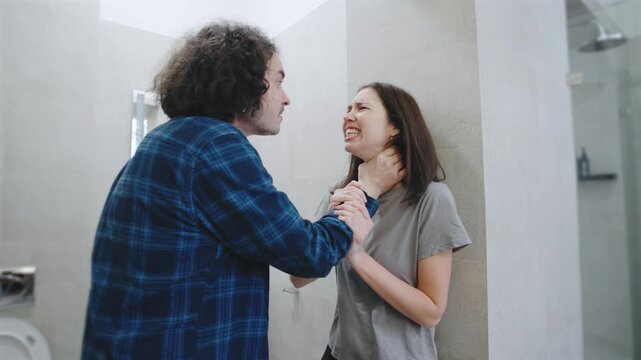 In a staged performance, a male actor yells while grabbing his on-screen partner by the throat in a bathroom, portraying a moment of fear and domestic violence. Two professional actors