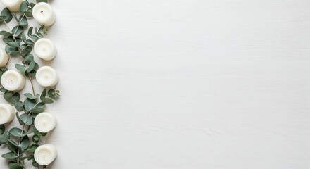 White candles and fresh eucalyptus branches are neatly arranged along the left side of a clean, minimalist white wooden table, offering ample copy space from a top-down perspective.