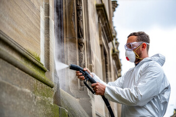 Worker in protective suit power washing historic stone building facade