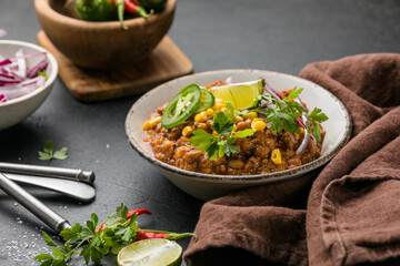 Chili con carne on wooden table with corn and spices