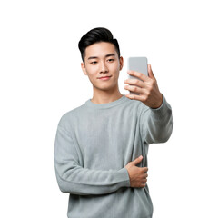 Fototapeta premium Young Asian man in a light blue sweater taking a selfie with his smartphone, smiling casually in a studio setting.