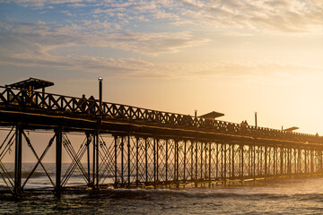 Fototapeta premium Tourists walking along the pier at sunset in Pimentel, Peru