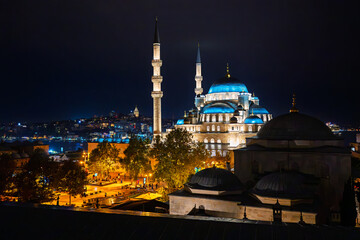 Naklejka premium The illuminated Yeni Mosque, also known as the New Mosque, with the Galata Tower and Bosphorus Sea Strait in view behind, in Istanbul, Turkey.