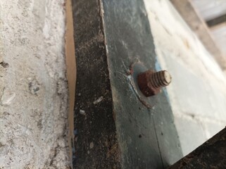 Close-up photo of a rusty bolt on metal and concrete wall, showing texture, corrosion, and industrial detail with natural lighting and sharp focus.