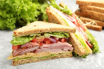 Delicious sandwiches with ham, cheese and vegetables on grey textured table, closeup