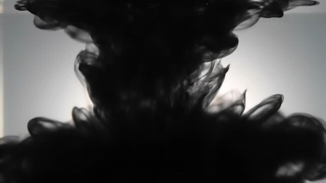 A dense cloud of black ink slowly disperses and swirls within transparent liquid, creating organic, evolving abstract shapes against a gentle, diffused light.