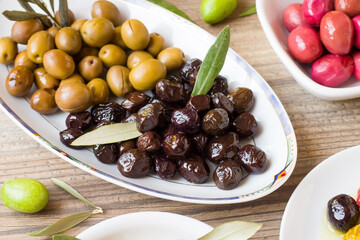 Ripe black and green olives, arranged on the same white plate, on a wooden background