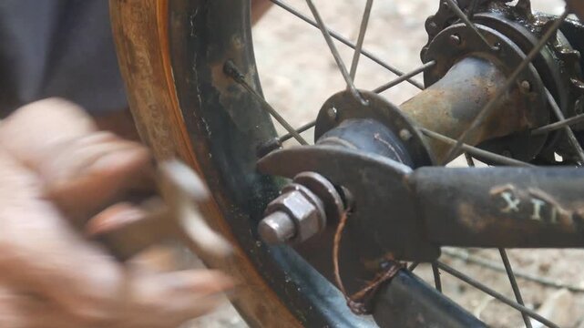 Close up of an old man's hand doing repair work on a child's bicycle wheel using a wrench.
