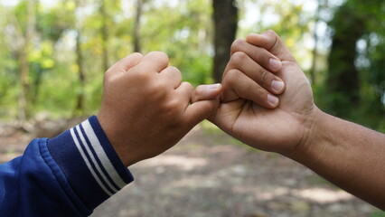 Two people link their pinky fingers in a symbolic gesture of a pinky promise or oath