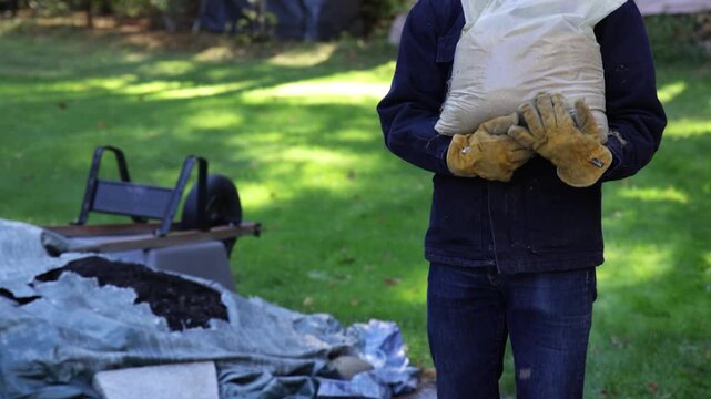 Landscaper With Yellow Gloves Carrying Sandbag In The Fall