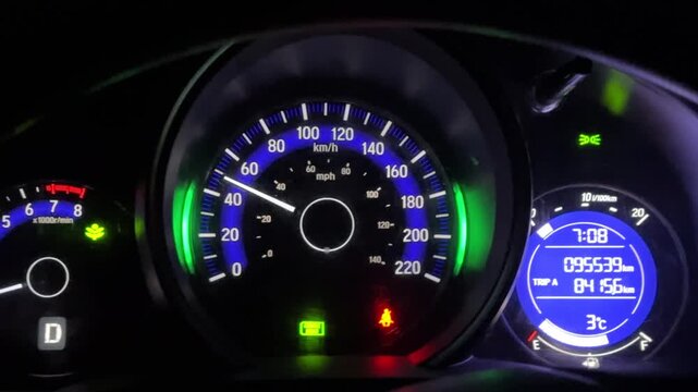 Automobile dashboard panel with illuminated speedometer, tachometer, and digital display, photographed in low light to emphasize the glowing gauges and modern car interior design.