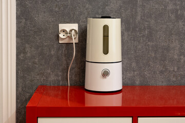 Air humidifier. An electric air humidifier stands on a red chest of drawers near a gray wall in a living room in an apartment. Close-up. Household appliances.