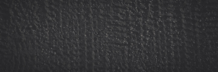 Texture of a decorative concrete wall. Rough dark gray surface with a grainy pattern of small stones and dents. Faded dark wide panoramic background for design. Shaded vintage texture with vignette.