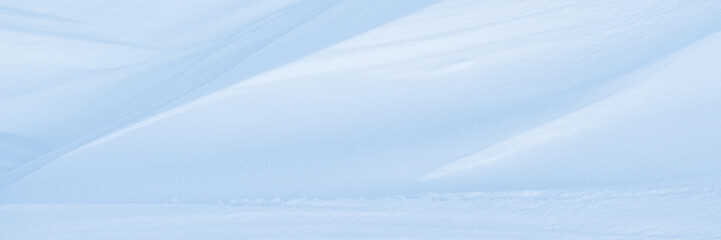 Beautiful winter background with snowy ground. Natural snow texture. Wind sculpted patterns on snow surface. Wide panoramic texture for background and design.