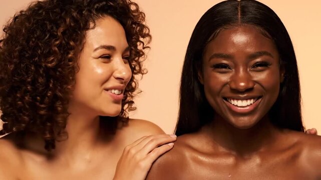 Two Smiling Women with Glossy Skin Posing Together in Front of Beige Background with Shoulder Touch Wearing Natural Makeup and Hair in Beauty Stock Photo Shoot with Studio Lighting