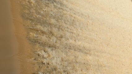 Abstract of fast-flowing, yellowish-brown water foaming and frothing as it rushes over an unseen...