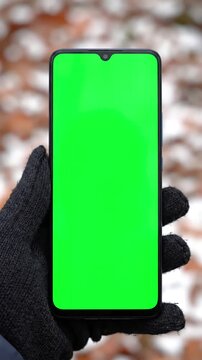 Autumn Digital Engagement with woman holds mobile phone and swipes photos or pictures outside on a cold day use vertical green screen for copy space closeup chroma key mock up smartphone in hand