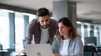 Collaboration and Guidance: A supportive scene unfolds as two colleagues work together, a mentor guiding a mentee through the intricacies of a laptop. The focus on teamwork and shared problem-solving.