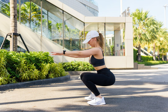 Fit woman performs challenging sport exercise workout outdoor, doing squats for strength training amidst modern city environment, fit individual embracing active healthy lifestyle for people - Powered by Adobe