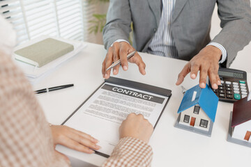 A real estate agent and client are discussing property purchase options, reviewing a contract, calculating loan terms, and considering house models as part of a housing investment decision.