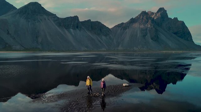 Visitors walk along the shoreline of Stokksnes Vestrahorn in Iceland, surrounded by majestic mountains and tranquil waters.