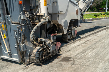 Large asphalt milling machine equipped with rotating drum and crawler tracks removing old pavement layer, preparing road surface for new asphalt application during city infrastructure upgrade © Andrei