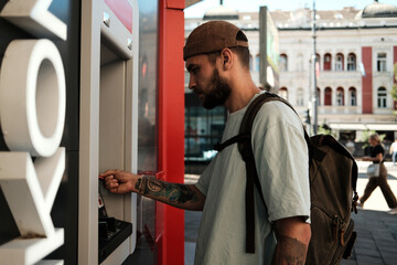 Young man standing at an ATM and inserting a card to withdraw money. Concept of finance, urban...
