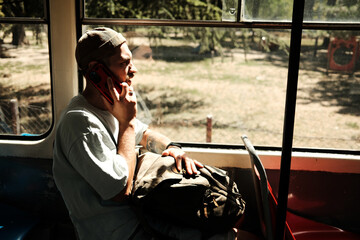 Young man sitting in a tram talking on smartphone during a daytime ride. Concept of communication, travel, and daily urban life. Side view portrait