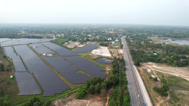 Aerial view of a large solar power plant next to a highway in rural Thailand, renewable energy landscape with solar panels and green surroundings.