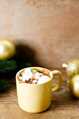 Hot chocolate in yellow cup on wooden table background.