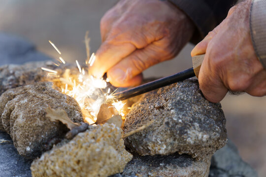 Bushcraft survivalist creating fire sparks with a ferro rod and cotton tinder, gathering heat outdoors
