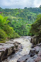 A beautiful landscape featuring the rushing waters of the Magdalena River surrounded by lush green hills in San Agustin, Huila, Colombia.