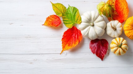 Vibrant autumnal scene featu colorful fall leaves and small decorative pumpkins arranged on a white wooden background