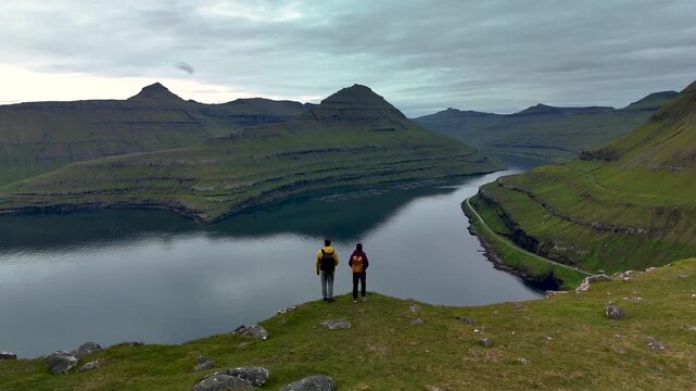 Discover the beauty of Gonguturur Hvithamar Trail in the Faroe Islands. Hikers enjoy panoramic views of lush green hills and tranquil waters, surrounded by dramatic landscapes. A true nature escape.