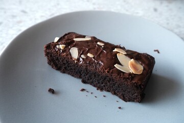 A rich, moist chocolate brownie topped with sliced almonds, served on a gray ceramic plate for a simple and indulgent dessert.
