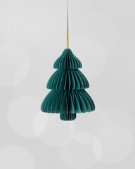 Minimal Christmas fir tree ornament of eco-friendly green paper hanging on golden string, on grey blurred bokeh background. Geometric shape stylish and natural look, holiday decoration trends.