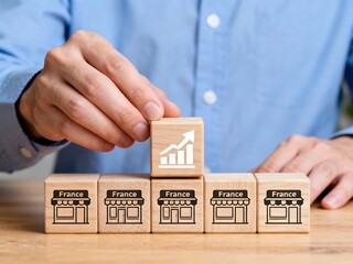France Business Growth Strategy Concept: Hand placing a wooden block with growth chart icon on top of shops labeled 'France', illustrating French market expansion and success
