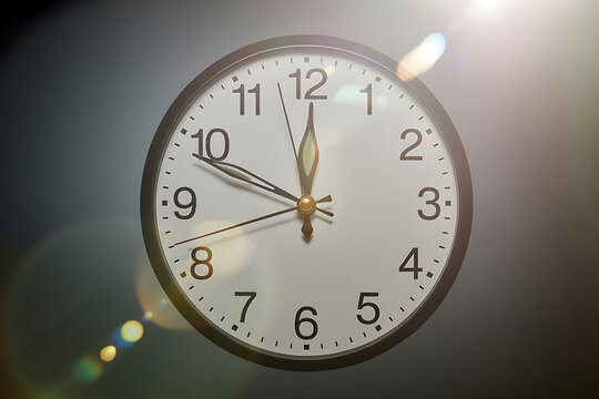 Close up of a classic analog clock face showing nearly midnight or noon with dramatic lens flare, symbolizing urgency and deadlines.