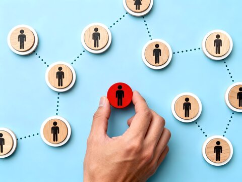 Hand adding red figure to social network made with wooden disks and dotted lines on a blue background Business concept for social connections, leadership, and recruitment
