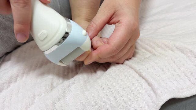 A woman using an electric foot file to remove calluses from her foot while sitting indoors