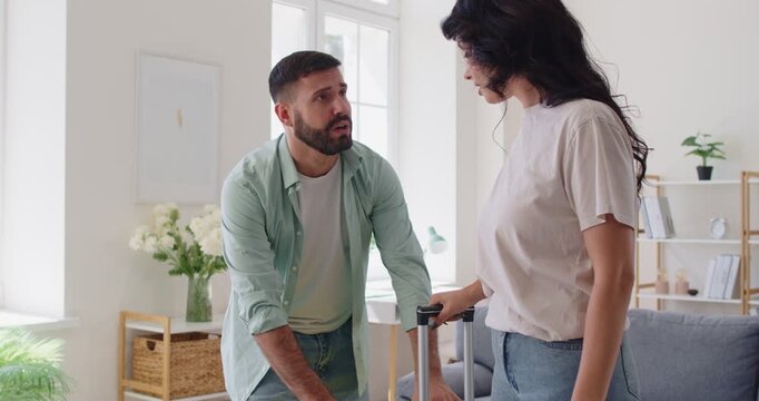 Couple breakup and relationship issues, begging man by suitcases of woman with pleas to stay at home. Young desperate boyfriend pleading with partner near luggage, asking girlfriend for forgiveness