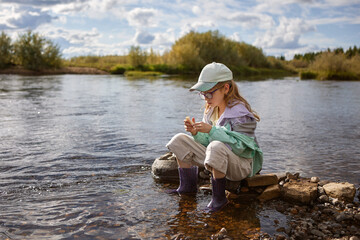 Little girl in mint jacket and cap sits by clear river water.
Sunlight reflects on pebbles creating peaceful countryside mood.
Candid outdoor moment shows childhood curiosity and nature calm.
