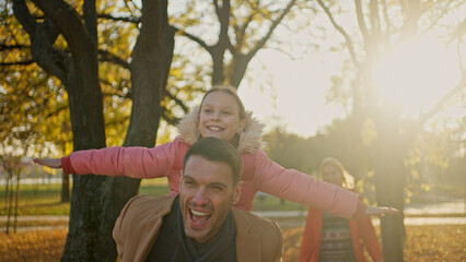 Father giving daughter a piggyback ride in a sunny autumn park